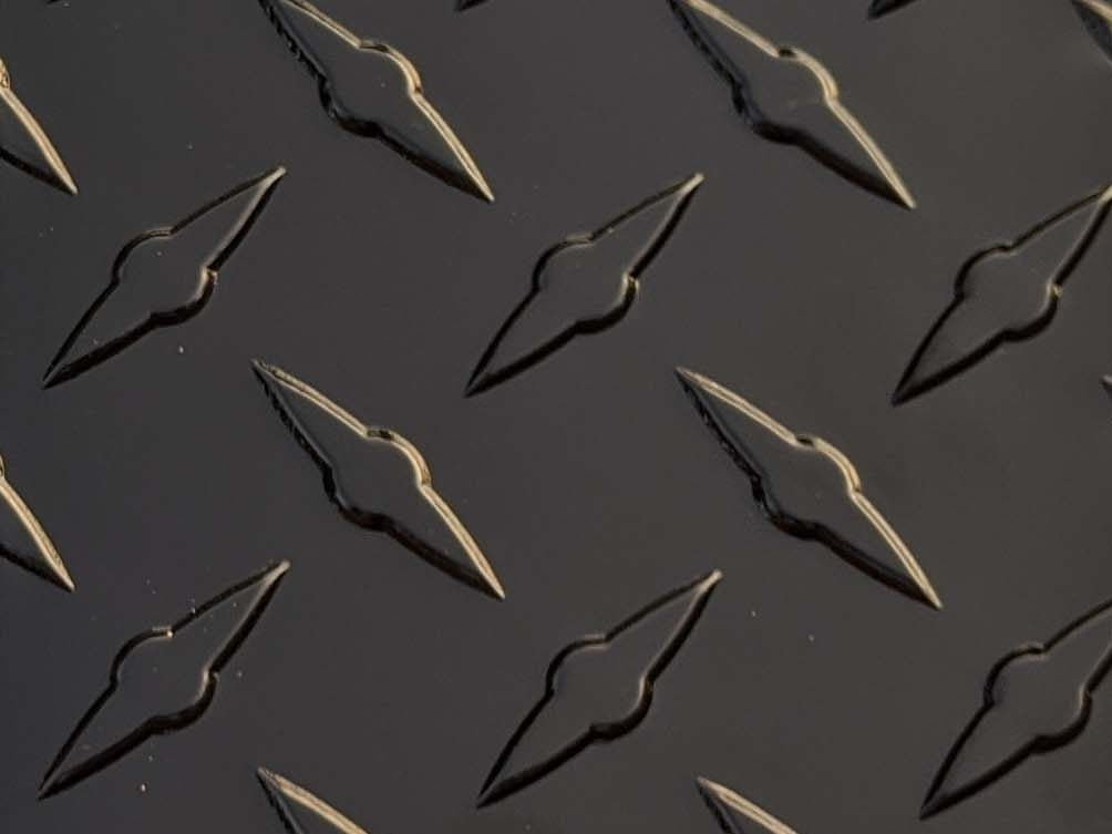 A large, black aluminum diamond plate sheet with a textured, raised pattern, backed with durable PVC material, measuring 49 inches by 96 inches.